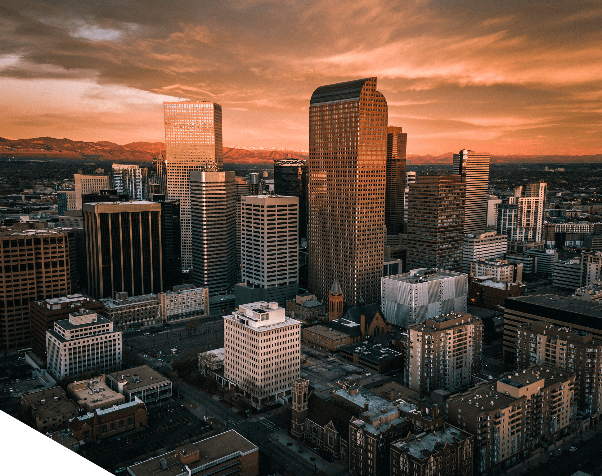 Aerial view of a city skyline at sunset, where the expertise of real estate experts is evident in the blend of tall skyscrapers and charming older buildings, all set against mountains under a partly cloudy sky.